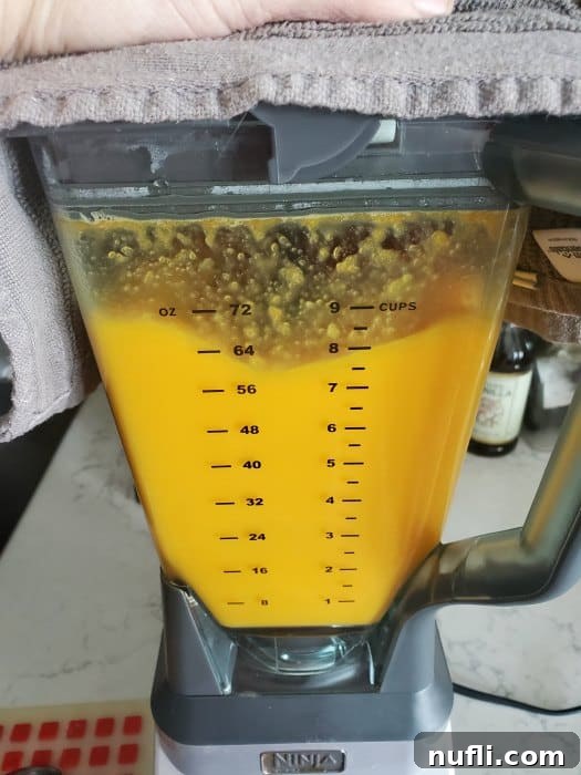 Orange liquid filling a blender, with a towel draped over the top to catch steam