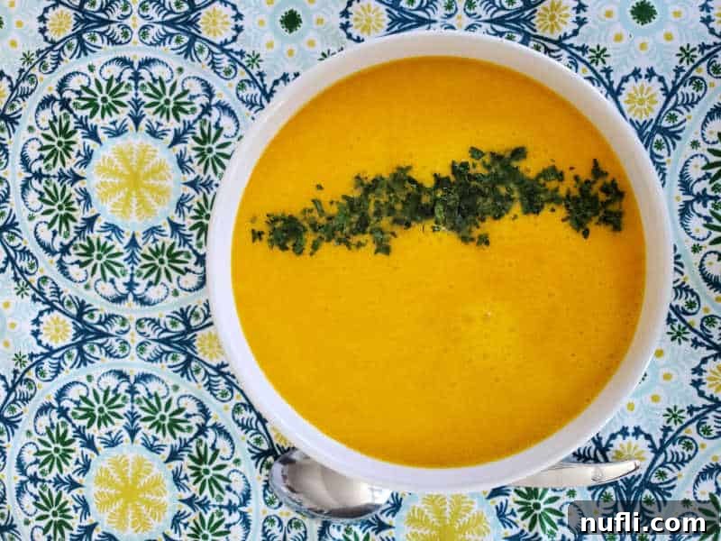 Creamy orange carrot soup with a swirl of green garnish in a white bowl, positioned on a vibrant patterned napkin