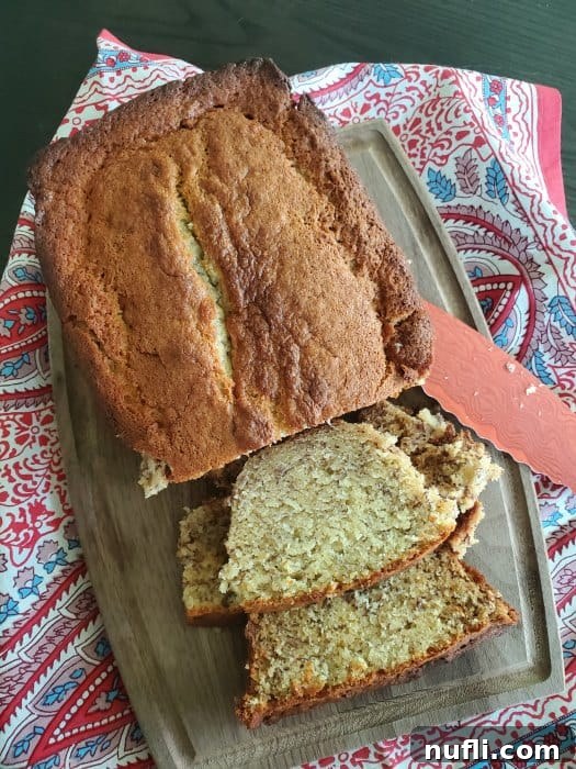 Close-up of a rustic wooden cutting board featuring perfectly sliced sour cream banana bread, arranged invitingly next to a sharp serrated knife.
