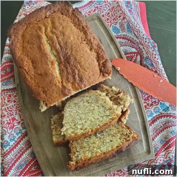 Loaf of sour cream banana bread with slices cut on a wooden cutting board with knife and cloth napkin