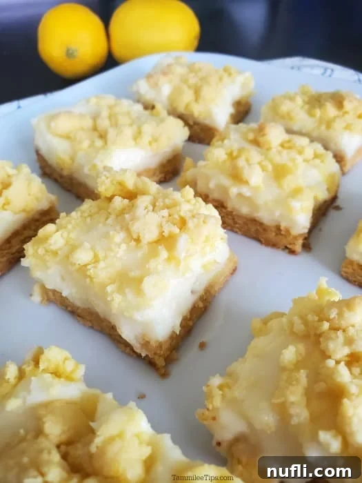 Perfectly cut Lemon Cheesecake Bar squares elegantly arranged on a white platter, with fresh whole lemons artfully placed in the background.
