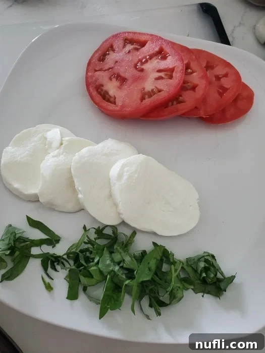 tomato slices, mozzarella cheese, and basil on a white plate