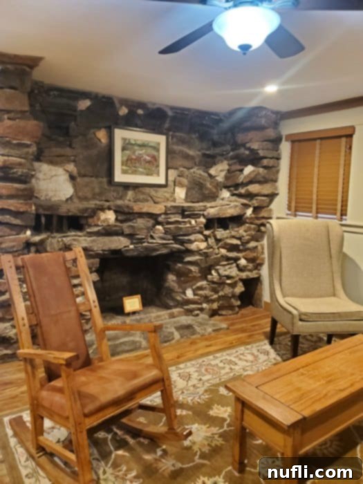 rock fireplace behind a rocking chair and cloth chair next to a long table 