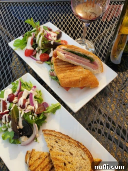two plates with paninis and salads next to a glass of wine