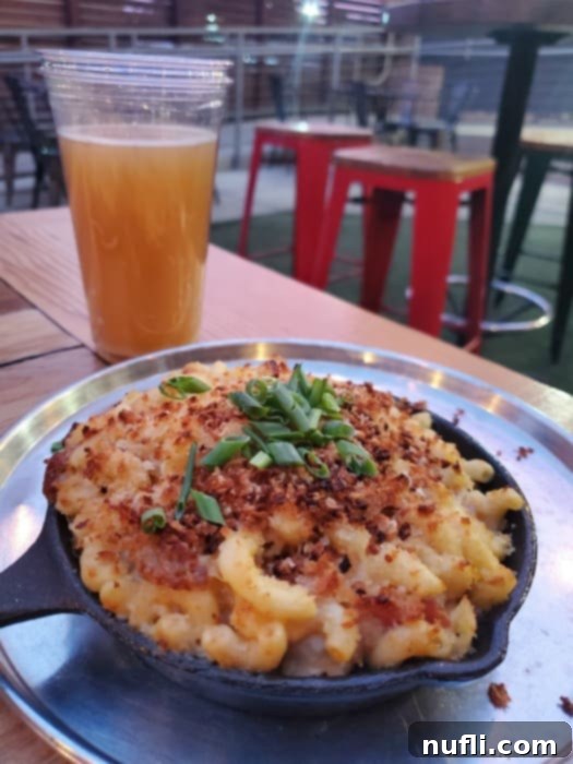 mac and cheese in a skillet next to a glass of beer on a picnic table 