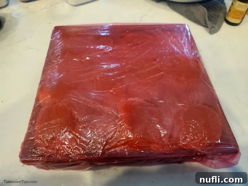Metal baking dish with Funeral Sandwich sliders wrapped in red plastic wrap, marinating in the refrigerator