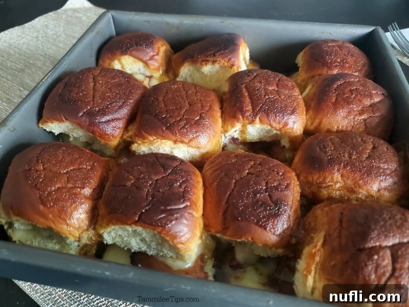 Close-up of baked ham and cheese Funeral Sandwiches in a metal baking dish, showing golden tops and melted cheese