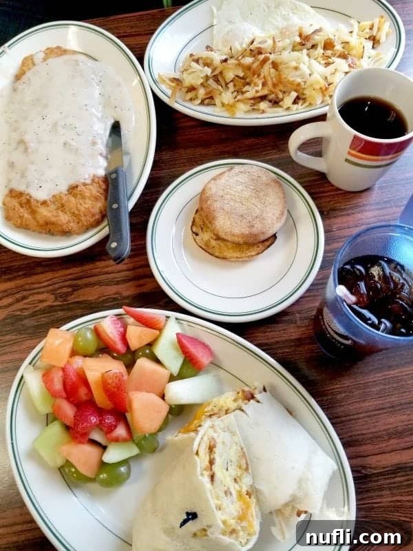 wooden table with plates of chicken fried steak, breakfast burrito, english muffin, eggs, and hashbrowns