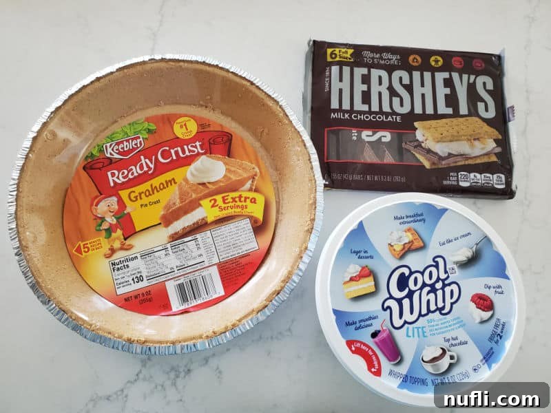 The three essential ingredients for the no-bake Hershey's pie laid out: a pre-made graham cracker pie crust, a tub of Cool Whip, and several classic Hershey's chocolate bars.