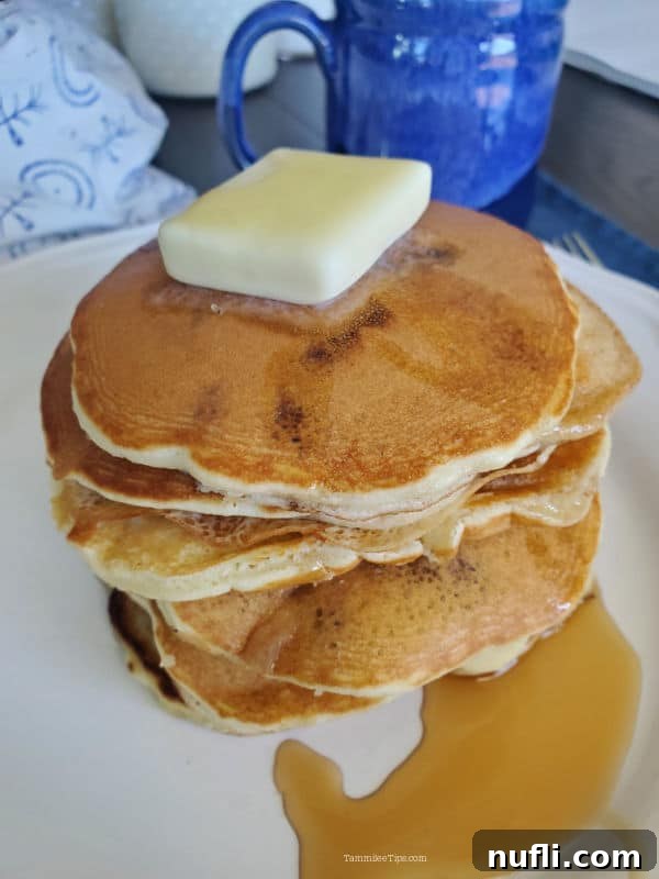 The 3 Ingredient Muffin Mix Pancake Hack 5 A stack of golden brown muffin mix pancakes on a white plate, positioned next to a rustic blue coffee mug filled with a warm beverage.