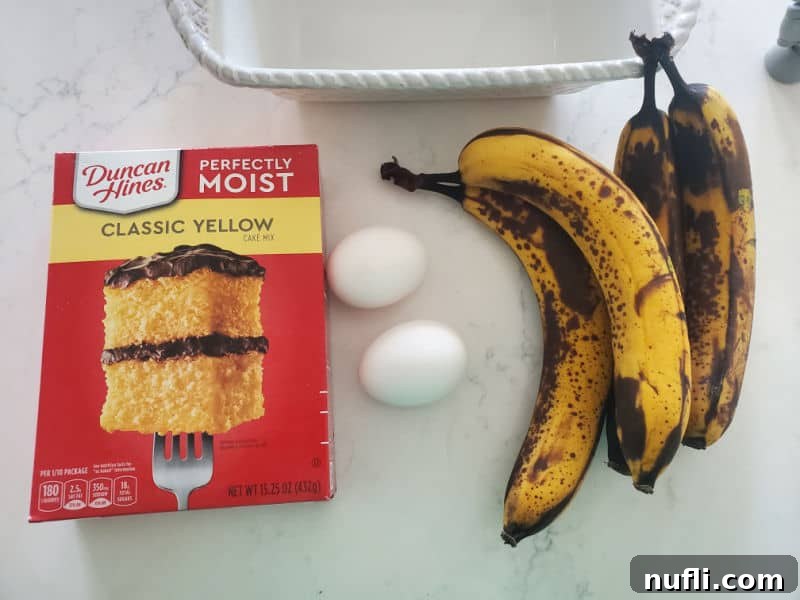 yellow cake mix box, eggs, and bananas on a white counter near a bread pan.