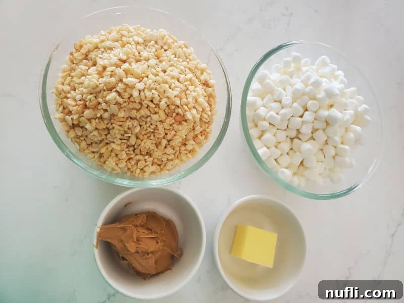 Delicious Peanut Butter Rice Krispie Treats 4 Four essential ingredients for Peanut Butter Rice Krispie Treats laid out on a white countertop: a bowl of Rice Krispies, a bowl of mini marshmallows, a small bowl of creamy peanut butter, and a small bowl of butter.