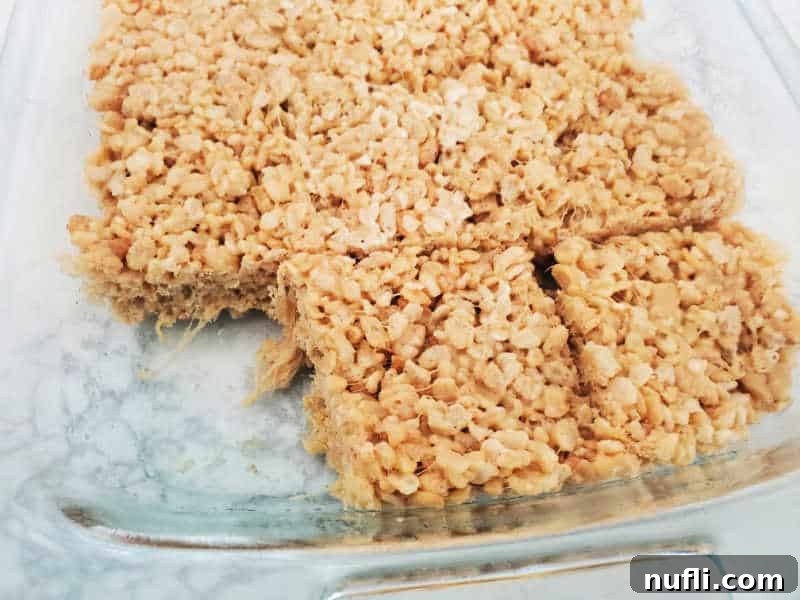 Delicious Peanut Butter Rice Krispie Treats 5 A glass baking dish filled with golden-brown Peanut Butter Rice Krispie Treats, with one square neatly removed from the corner, revealing the chewy interior texture.