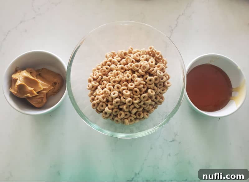 Bowls filled with peanut butter, Cheerios, and honey on a marble counter, ready for mixing