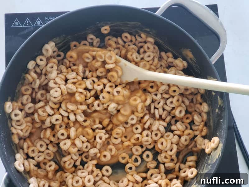 Peanut butter and Cheerios mixture in a pot, ready to be pressed into a baking dish