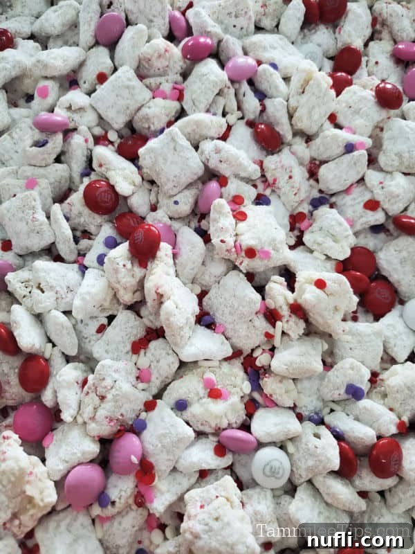 Close-up view of Valentine's Day Muddy Buddies, showcasing the powdered sugar coating, pink and red M&Ms, and festive sprinkles.