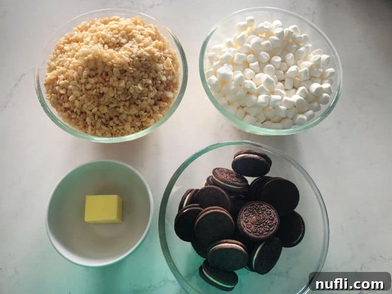Glass bowls filled with rice krispie treats, mini marshmallows, butter, and Oreo cookies