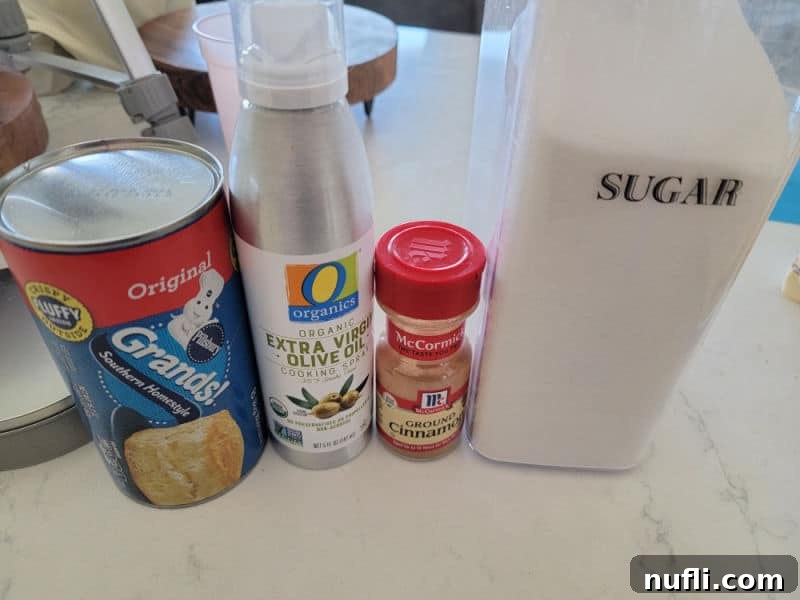 Air fryer Donuts ingredients, Grands Biscuits, Olive Oil Spray, Cinnamon, and Sugar on a white counter.