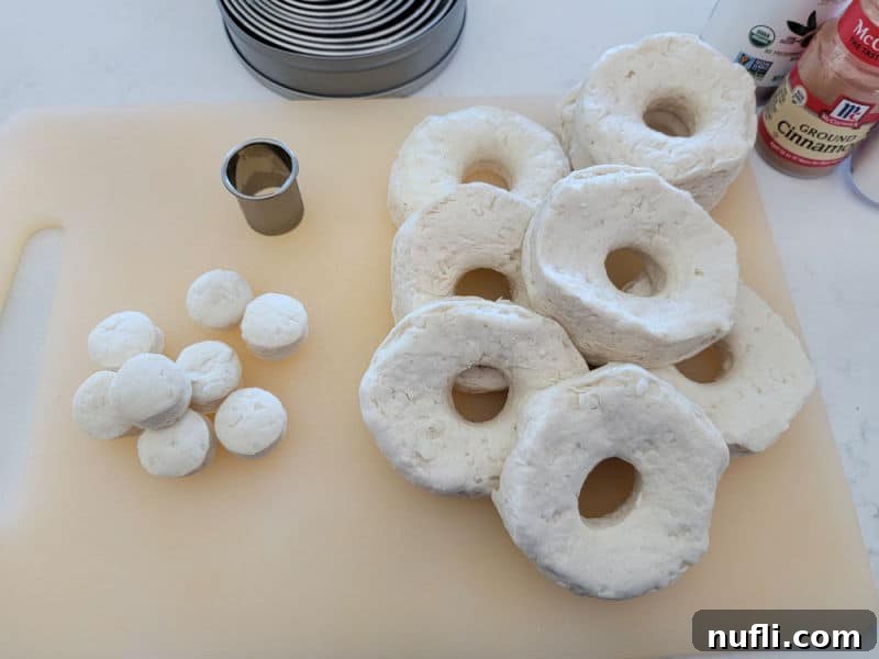 Air fryer donuts with a biscuit cutter on a cutting board before air frying.
