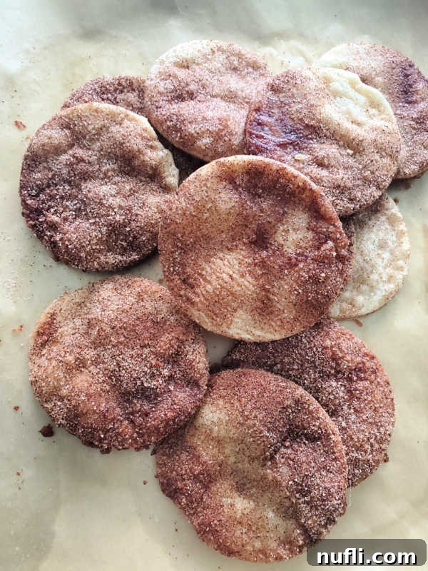 Freshly baked pie crust cookies, some cut into festive shapes, cooling on parchment paper on a baking sheet.