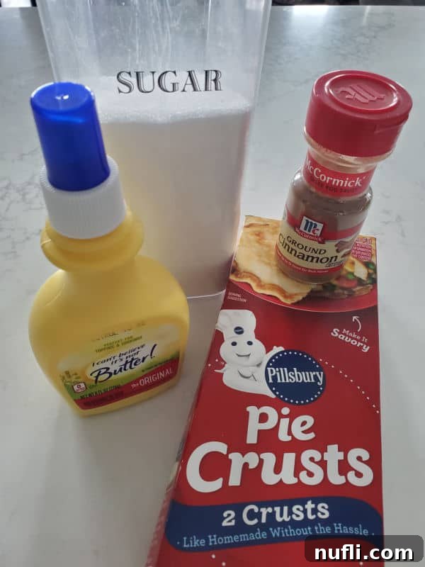 The four simple ingredients for pie crust cookies laid out: sugar, butter spray, a roll of pie crust, and ground cinnamon.