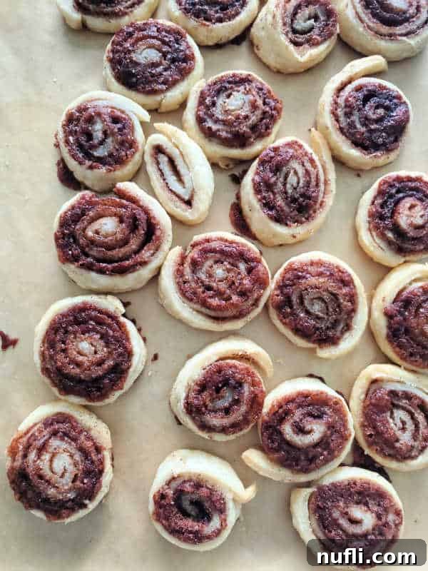 Neatly rolled pinwheel-shaped pie crust cookies, before baking, arranged on a baking sheet lined with parchment paper.