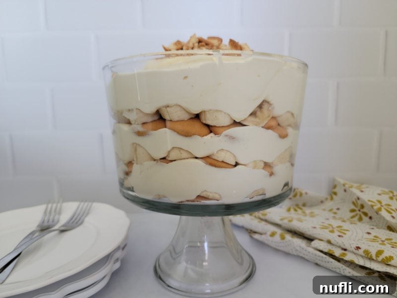 A trifle dish displaying the beautiful layers of banana, Nilla wafers, and pudding, with plates and forks ready.