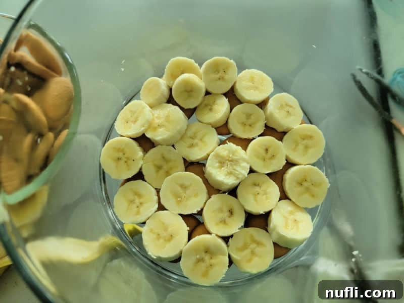 A layer of sliced bananas spread over Nilla wafers in a glass trifle dish.