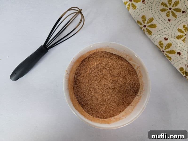 Cinnamon Sugar in a white bowl next to a whisk and cloth napkin