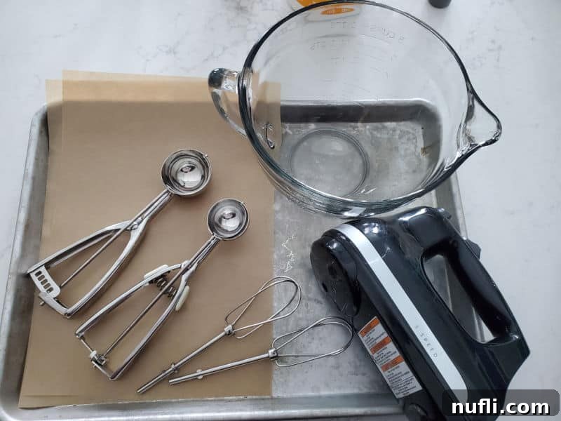 Cookie scoops, hand held mixer, glass batter bowl, parchment paper, and baking sheets