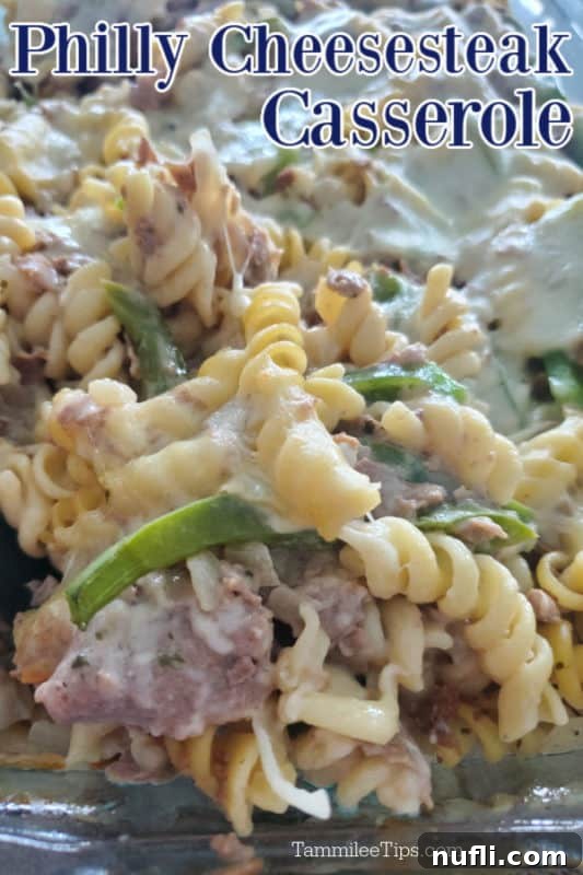 A large glass baking dish filled with golden-brown Philly Cheesesteak Casserole, featuring tender steak, al dente pasta, melted provolone cheese, and vibrant green bell peppers.
