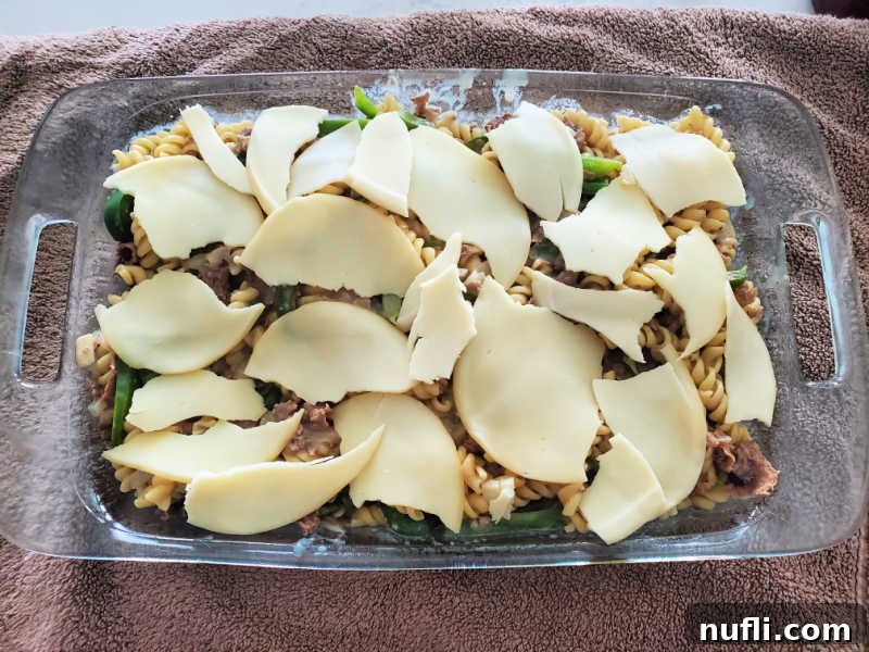 Layers of provolone cheese slices covering the top of a bubbling Philly Cheesesteak Casserole in a baking dish, ready for the oven.