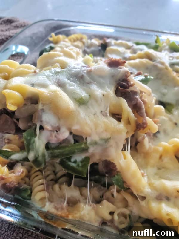 Close-up of a spoon lifting a portion of hot Philly Cheesesteak Casserole, with stringy, melted provolone cheese stretching deliciously.