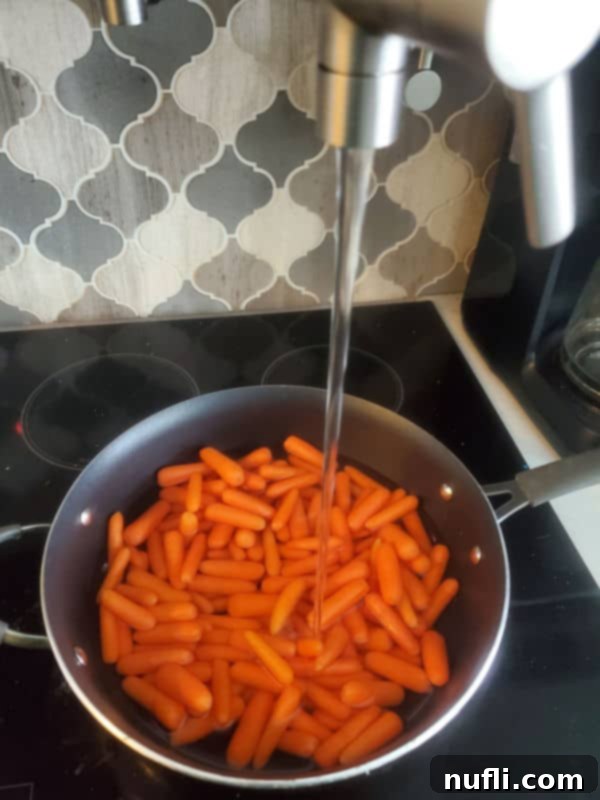 Cracker Barrel Copycat Carrots 4 Baby carrots in a sauce pan with water flowing from a pot filler above on the stove top