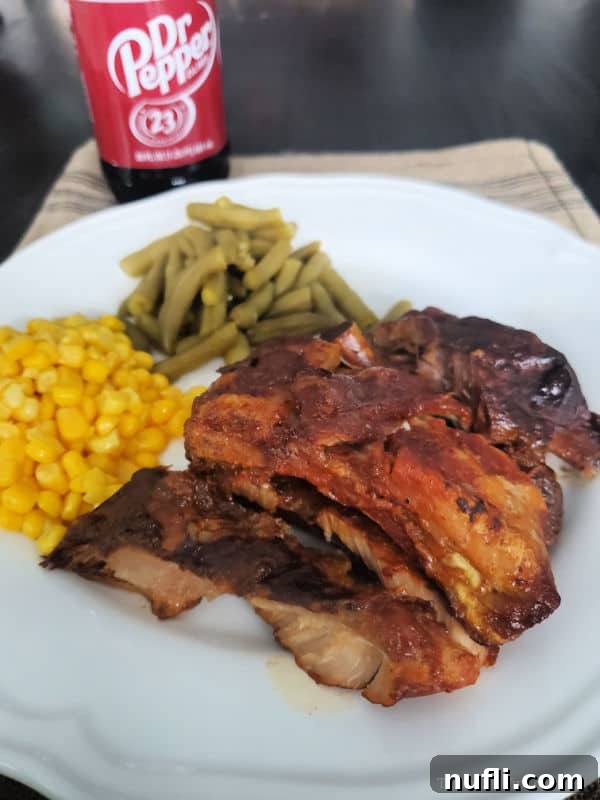 A beautifully plated serving of Dr. Pepper Crock Pot Ribs, adorned with fresh green beans and sweet corn, ready to be enjoyed.