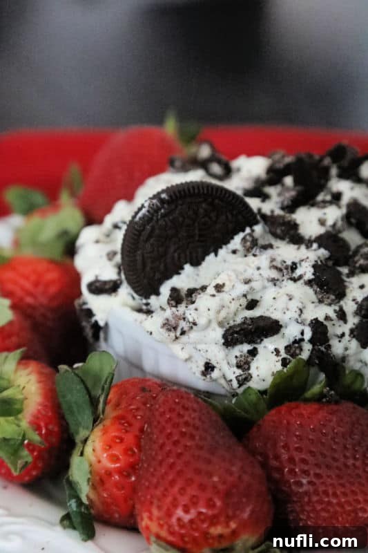 Oreo Fluff salad in a white bowl with cookies and cream garnish next to strawberries