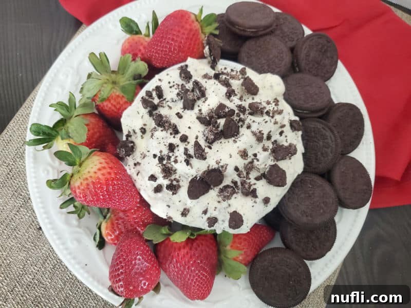Oreo Cookie Fluff in a white bowl on a white plate with Strawberries and oreo Cookies next to a red napkin