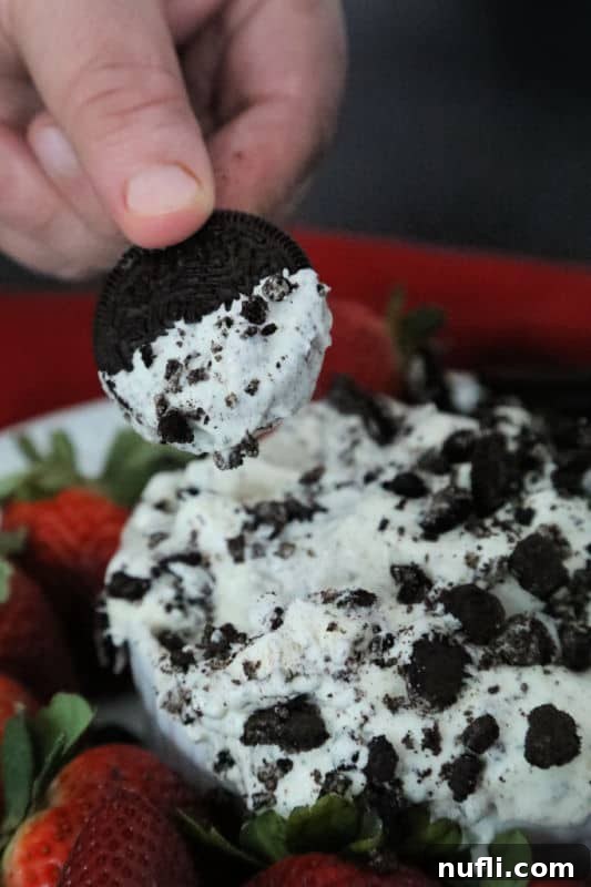 Oreo cookie dipping into Oreo fluff next to strawberries