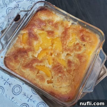 Bisquick Peach Cobbler in a glass baking dish by a cloth napkin