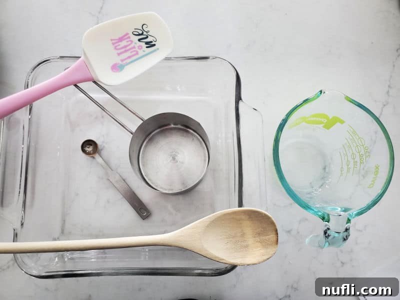 Spatula, wooden spoon, measuring tools, glass baking dish, and measuring cup on a white counter. 