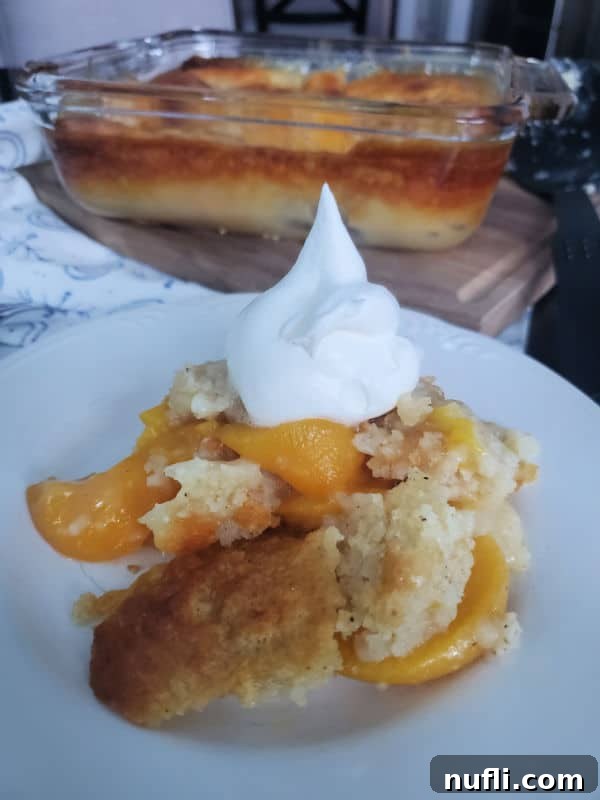 peach cobbler with a dollop of whipped cream on a white plate with a baking dish in the background
