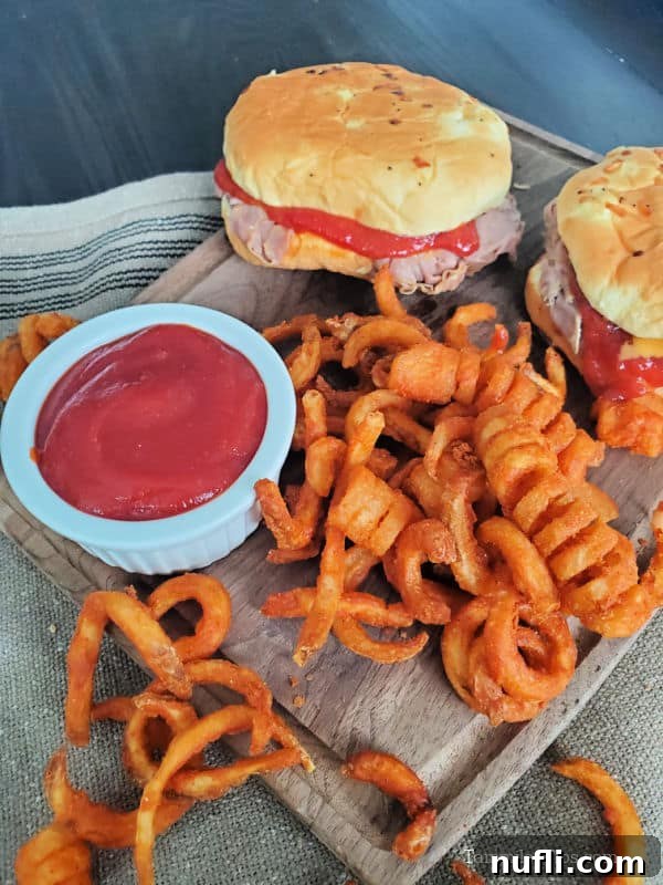 Arby's sauce in a white bowl next to curly fries and two Arby's roast beef sandwiches. 