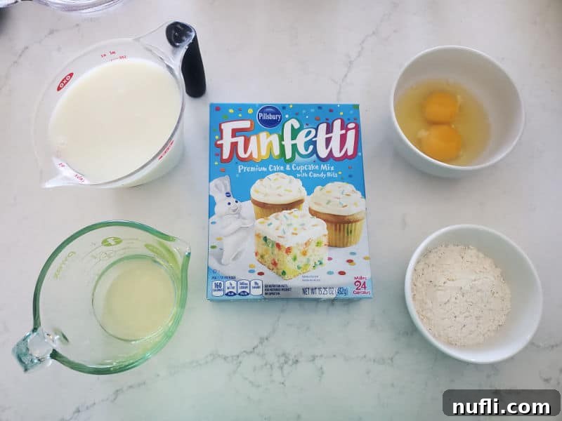 Essential ingredients for Funfetti Cake Mix Pancakes laid out on a white counter: a box of Funfetti cake mix, fresh eggs, a carton of milk, and a bottle of vegetable oil.