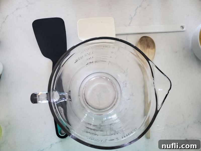 glass batter bowl, spatula, wooden spoon, and pancake turner on a white counter 