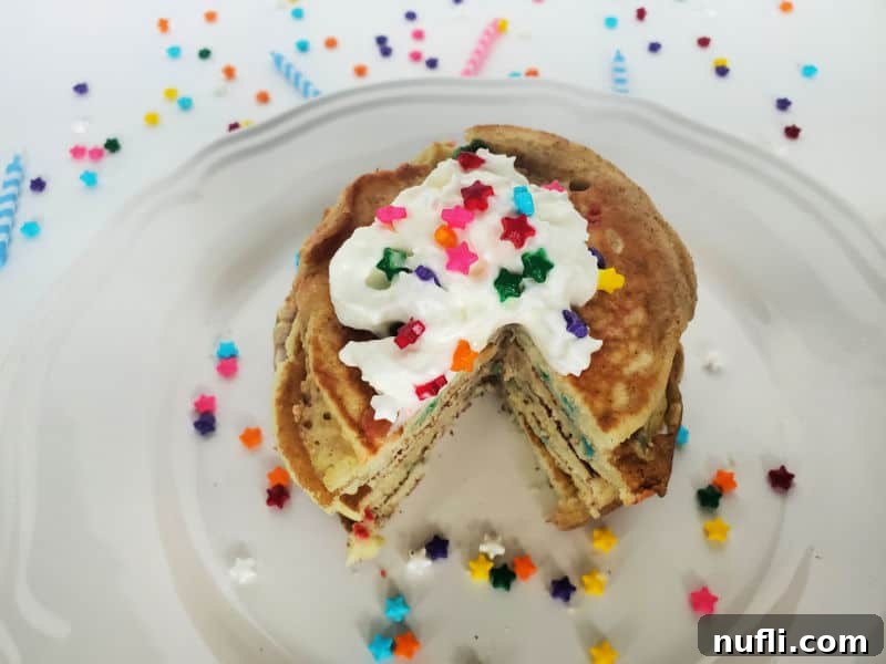 Funfetti Pancakes on a white plate with sprinkles and whipped cream