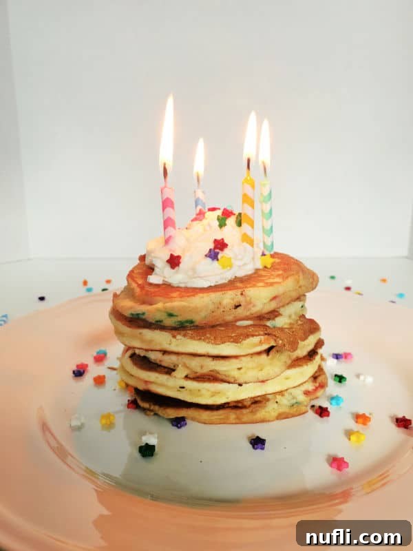 Stack of funfetti cake mix pancakes with lit birthday candles, whipped cream, and sprinkles on a white plate