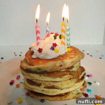 Stack of Funfetti Cake Mix Pancakes on a white plate with lit birthday candles, whipped cream, and sprinkles.