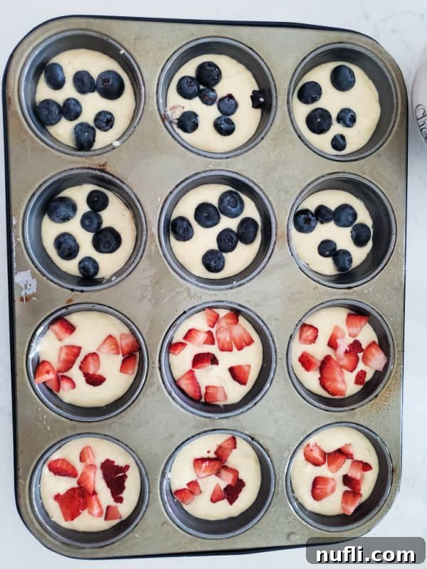 A muffin tin filled with unbaked pancake muffin batter, some with blueberries visible, ready to be placed in the oven.