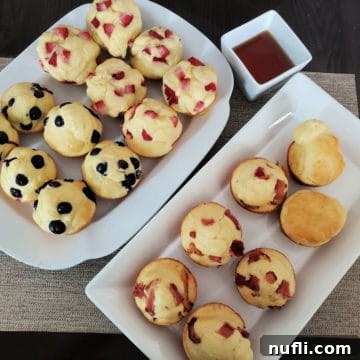 A tantalizing display of pancake muffins on white platters, adorned with various toppings like fresh berries and chocolate chips, accompanied by a bowl of syrup.