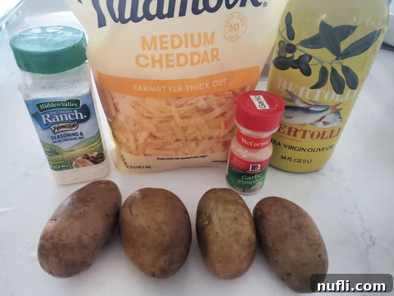 Cheesy Ranch Potatoes ingredients, hidden valley ranch mix, cheddar cheese, garlic powder, olive oil, and russet potatoes on a white counter